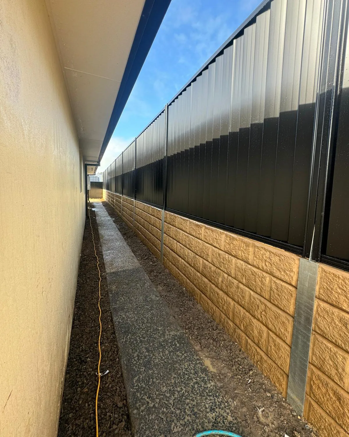 Black Colorbond steel fencing above sandstone-finish concrete sleepers